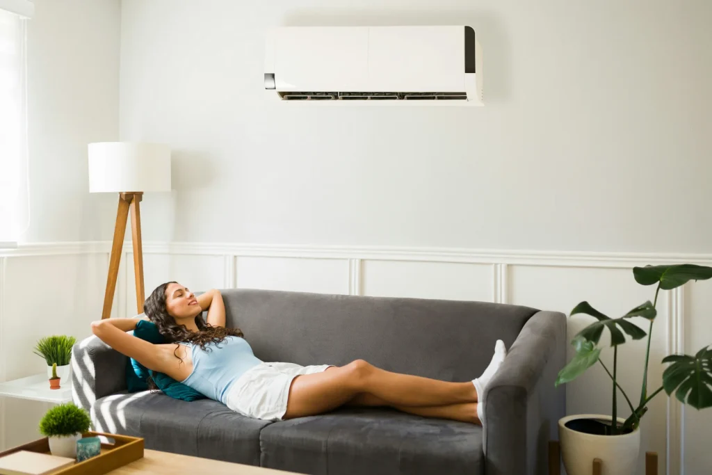Image of a woman relaxing on a couch under a clean, wall-mounted AC unit in a well-maintained home